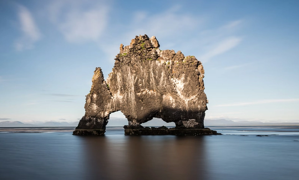 Rock monolith surrounded by body of water.